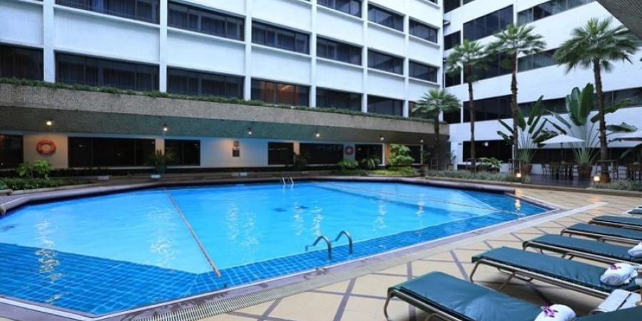 Scenic view of the pool at Asia Hotel Bangkok, adorned with lounge chairs and lush palm trees for a serene atmosphere.